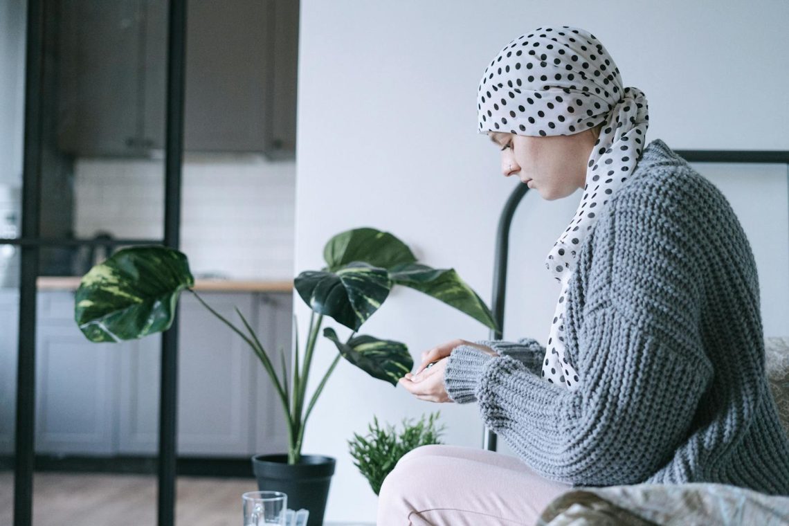 Woman in headscarf sitting indoors, taking medication, symbolizing cancer care and support.