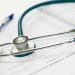 A stethoscope and pen resting on a medical report in a healthcare setting.