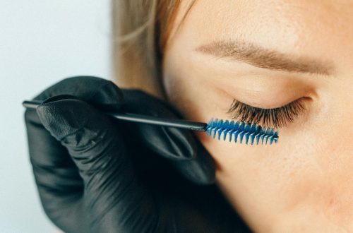 A professional applying eyelash extensions using a blue applicator brush for a refined look.