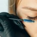 A professional applying eyelash extensions using a blue applicator brush for a refined look.